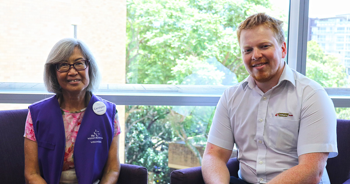The Wesley Hospital Volunteer and Staff member sitting on separate couches posing for photo