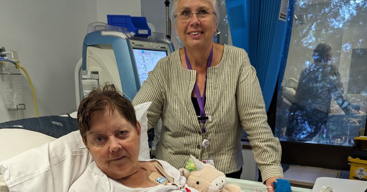 Volunteer Compassionate Companion Lyndie Mitchell stands beside a patient, Vicky, who is lying in bed.