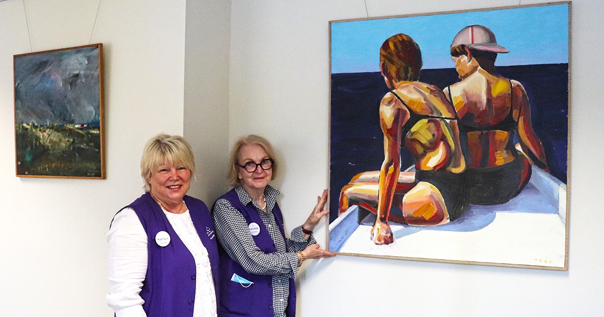 Two Wesley volunteers standing beside a piece of artwork.