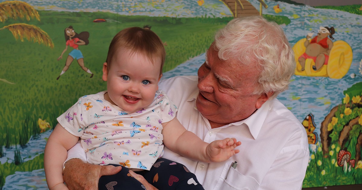 Dr Bruce Lewis smiling at a baby in front of a painted mural wall