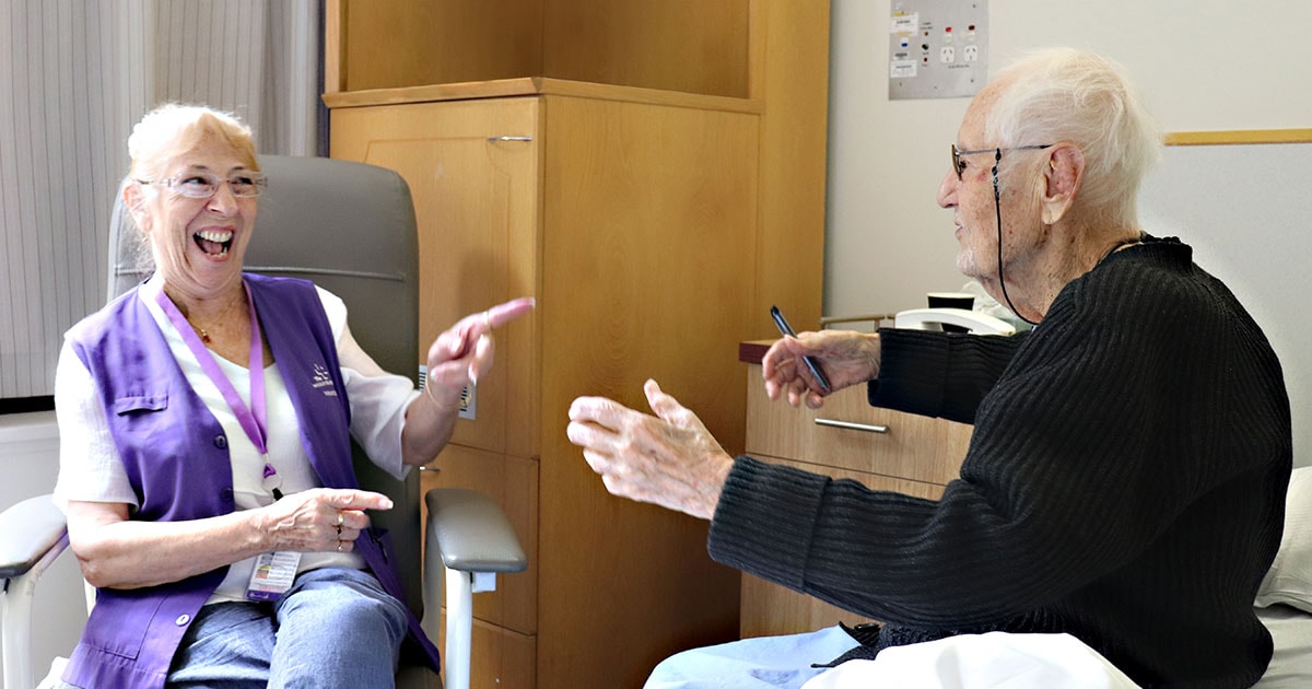 The Wesley Hospital Compassionate Companion volunteer smiling and pointing to a patient in bed