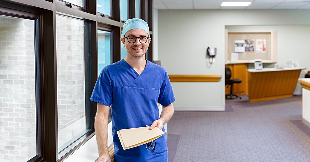 Dr Rhett Morton wearing scrubs standing in the hospital coridor holding a folder