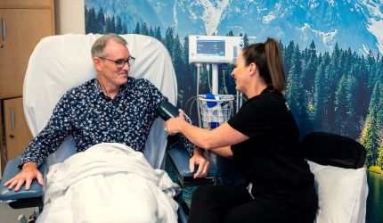 A nurse takes the blood pressure of a man sitting in a hospital chair.