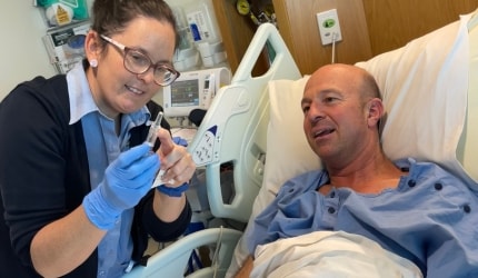 A patient receiving cancer treatment is listening attentively as a Wesley nurse gently explains the purpose and function of a piece of hospital equipment