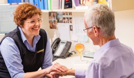 A Wesley team member is gently holding the hand of an older gentleman as they chat in a hospital office