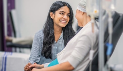 A young woman is talking to a patient receiving cancer treatment in a hospital room