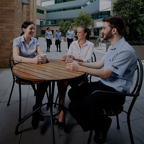 Be you – Three young Graduate Nurse Program participants share a laugh in a Wesley Hospital courtyard, as other medical staff approach.