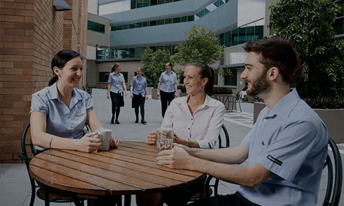 Be you – Three young Graduate Nurse Program participants share a laugh in a Wesley Hospital courtyard, as other medical staff approach.