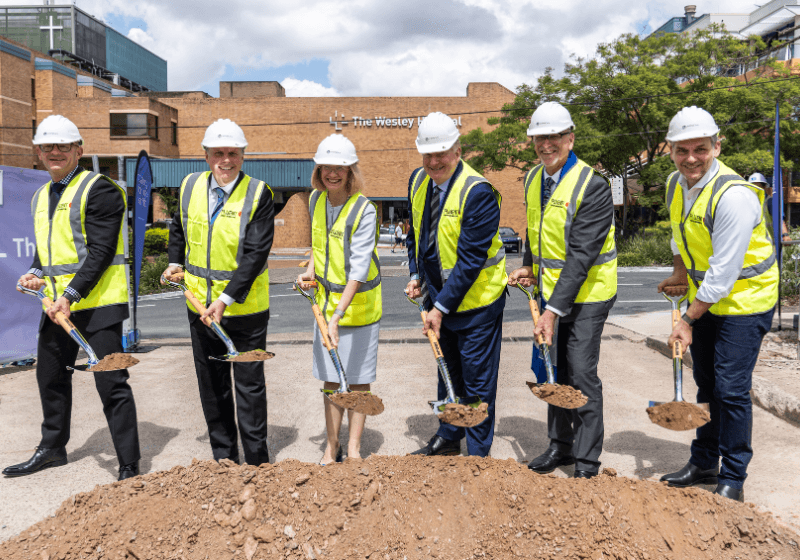 A group of men and women in high-vis vests, with shovels, turning the sod at the Wesley Expansion site.