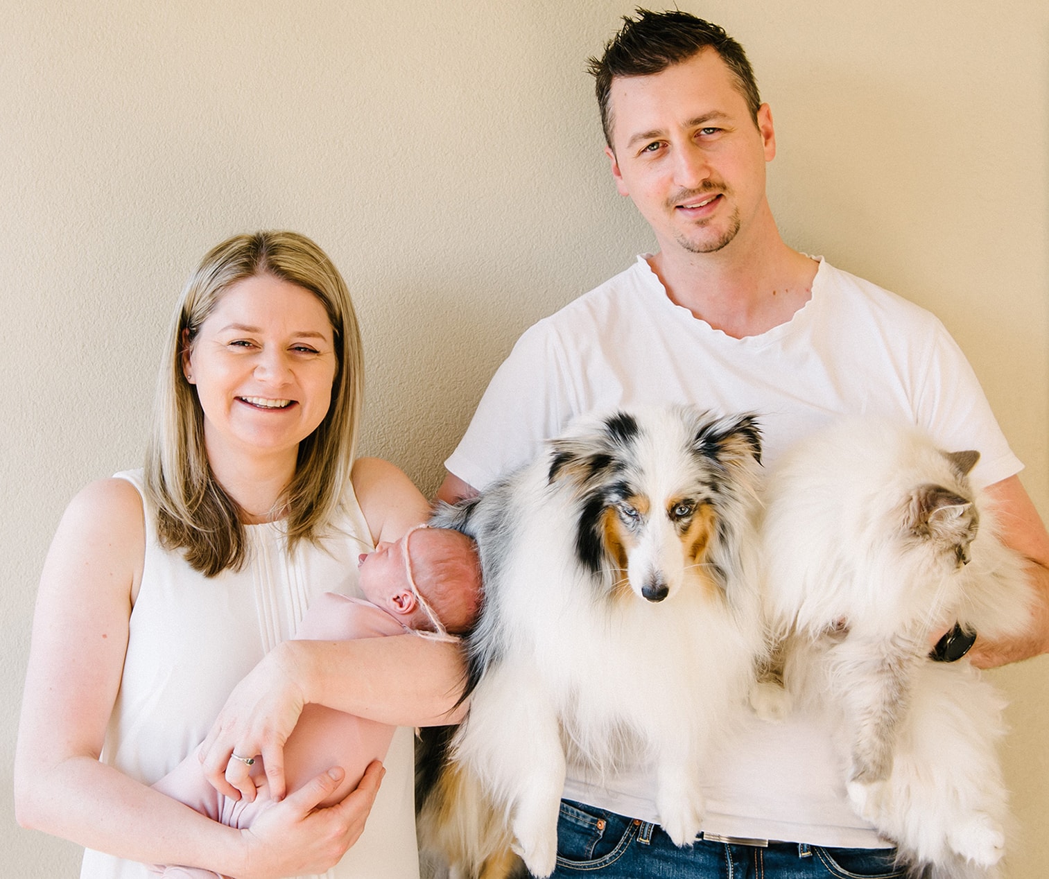 Kat Goodal A smiling woman holding a new born baby next to a man holding a dog and a cat